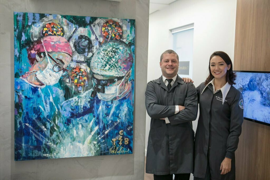 Dr. Rafael Belmonte e da Dra.Karina Tiemi Yoshizaki ao lado de uma pintura que retrata os dois em um procedimento